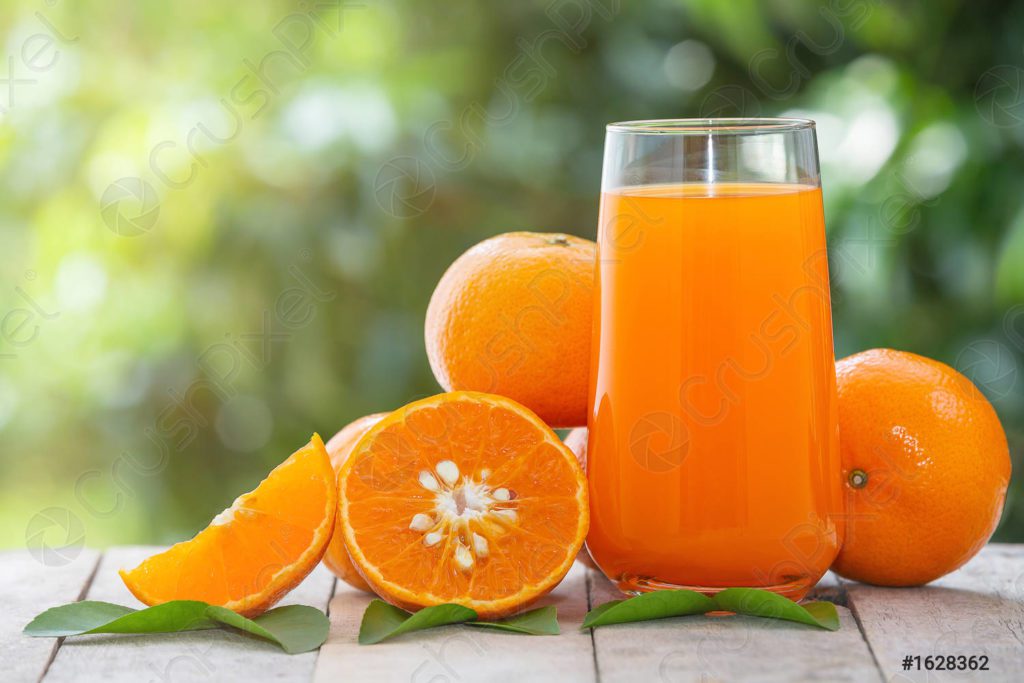 Kraj case pune soka od pomorandže stoje dve pomorandže, polovina pomorandže i jedna kriška