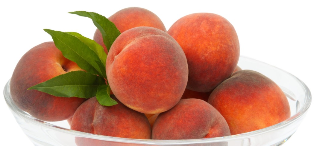 Staklena činija puna zrelih breskvi i nekoliko zelenih listova