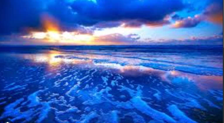 Pun mesec iza tamnih oblaka na plavom nebu odslikava se u moru i morskoj peni