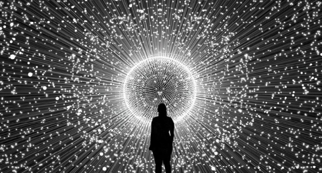 Crna silueta zene koja stoji ispred belog kruga svetlosti i mnostva belih tackica na crnoj pozadini